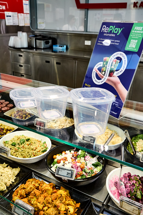 Display of pre-portioned meals in containers with a RePlay promotional sign in the background.