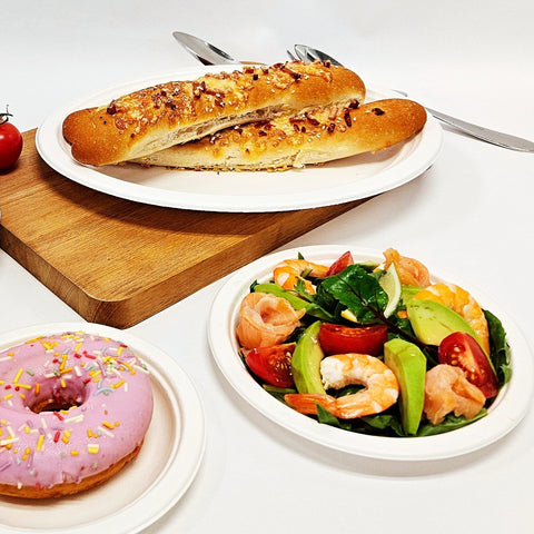 Three sugarcane oval and round plates with a sandwich, salad, and pink donut on a white background 