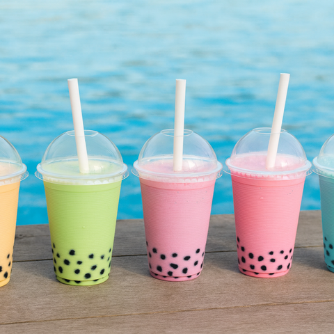 Colorful bubble tea drinks with straws on a wooden surface by a pool.