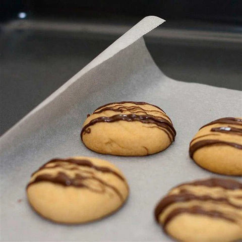 Cookies with chocolate drizzle on a baking tray lined with Silicone Baking Sheets.