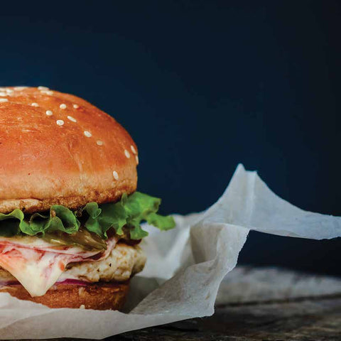 Hamburger with lettuce and cheese on a bun, sitting on white greaseproof paper placed on a dark background