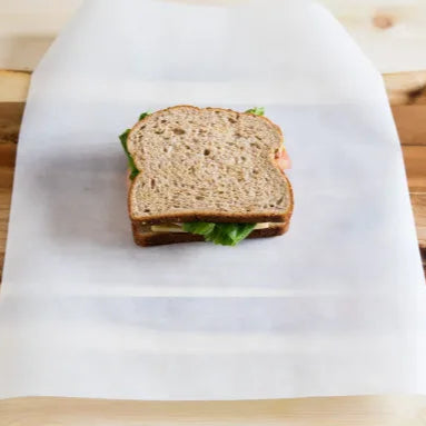 Unwrapped sandwich on a piece of white lunch wrap paper with a wooden surface underneath