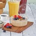 Container of oatmeal with berries on a wooden board, next to a glass of orange juice.