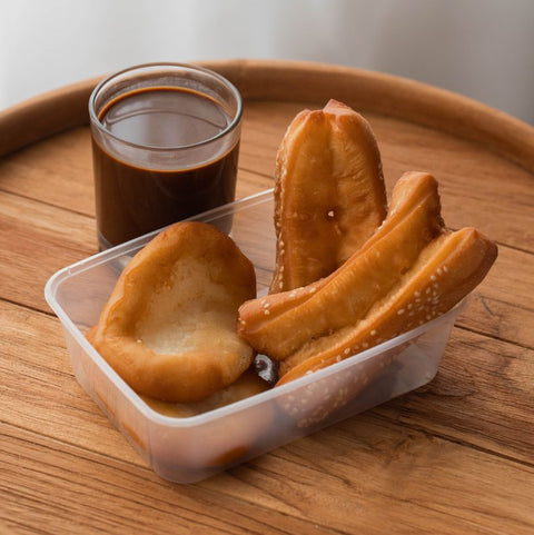 Bread rolls in a small plastic takeaway container with a glass of dark liquid on a wooden tray