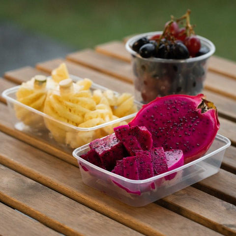 Dragon fruit slices and pineapple pieces in a container on a wooden table with a blurred background