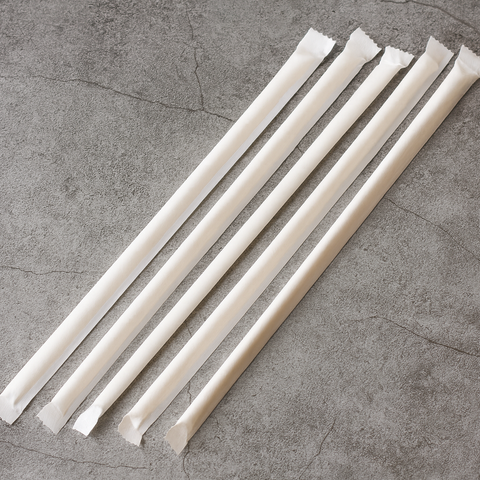 Set of white paper straws in paper wrap on a gray concrete surface
