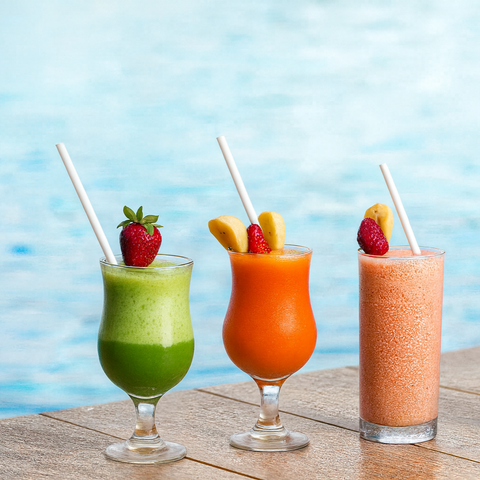 Three colorful smoothies in glasses with white paper straws against a blue water background